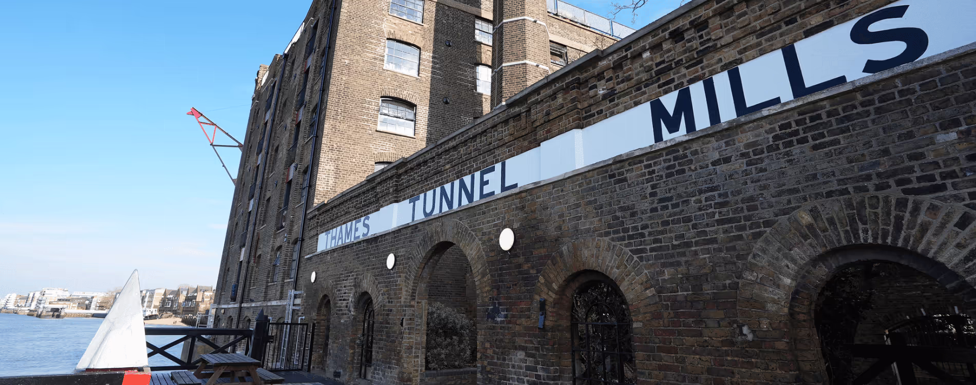 The historic Grade II listed Thames Tunnel Mills building, a former warehouse converted to residences, viewed from the riverside on a sunny day.
