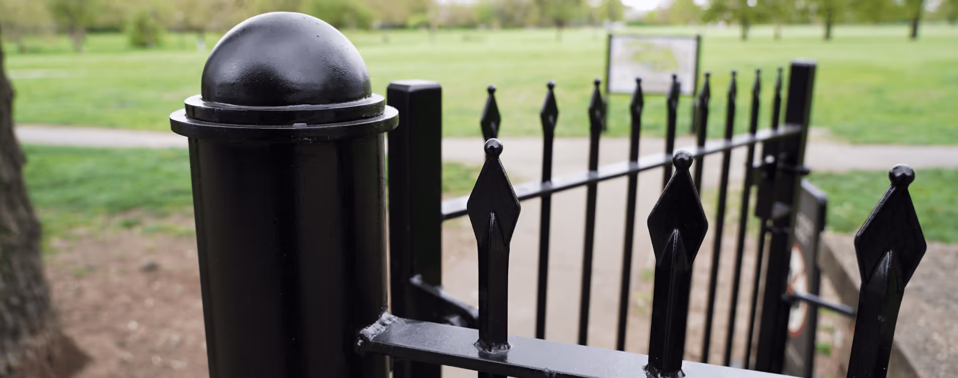 A close-up of a newly refurbished, black-painted heritage gate and railings at the entrance to a Royal Park, showcasing specialist conservation work.